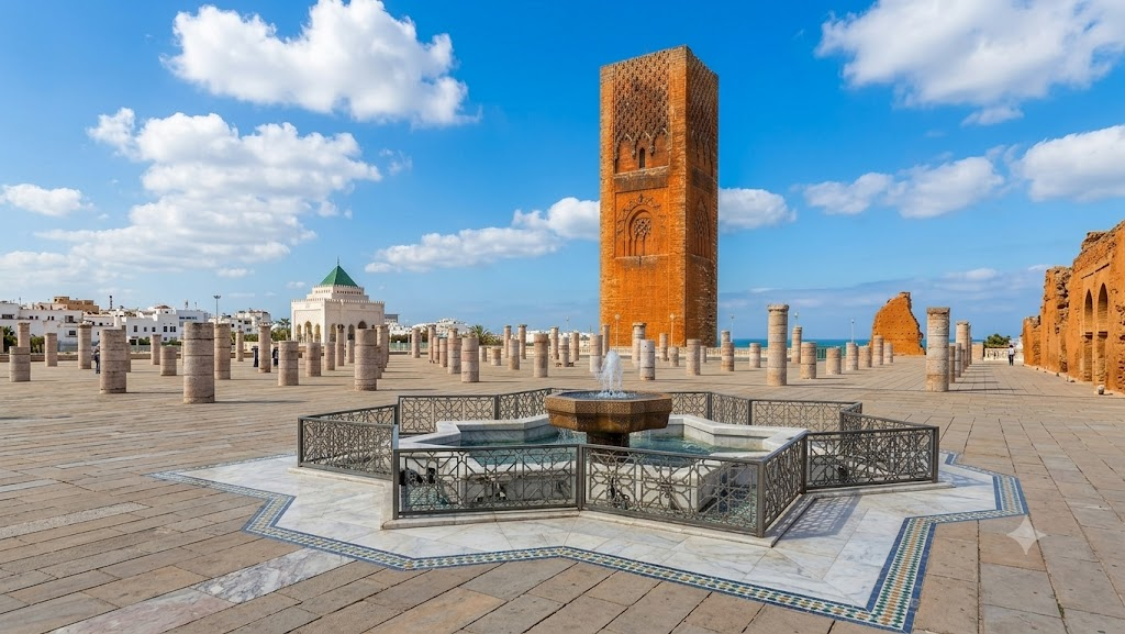 Tour Hassan, Esplanade et Fontaine à Rabat Vue panoramique de la Tour Hassan à Rabat avec son esplanade de colonnes historiques, la fontaine au premier plan et un ciel bleu nuageux.